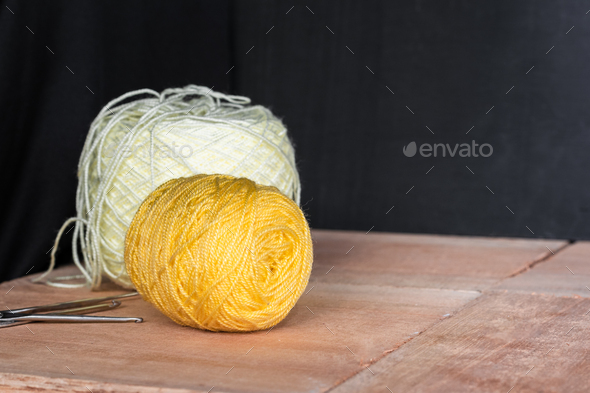 two rolls of yellow and white yarn to crochet, on a black and orange wooden  background. Stock Photo by mauriciotoro10