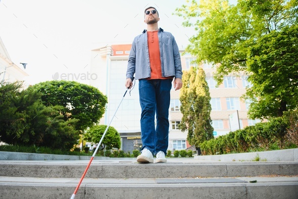 Young blind person with long cane walking in a city Stock Photo by