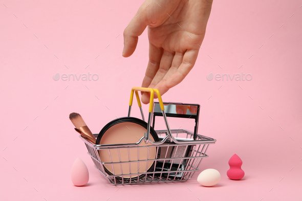 Shopping basket with decorative cosmetics, on a pink background.