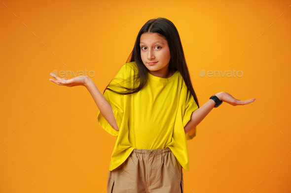 Puzzled teen girl don\'t know what to do on yellow background in studio