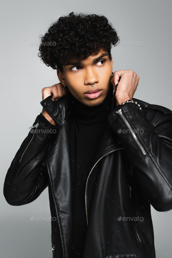 brunette african american man adjusting collar of black leather jacket  isolated on grey