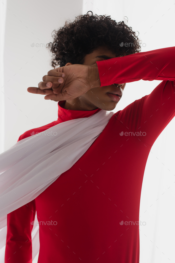 african american man in red turtleneck obscuring face with arm while posing in white chiffon cloth