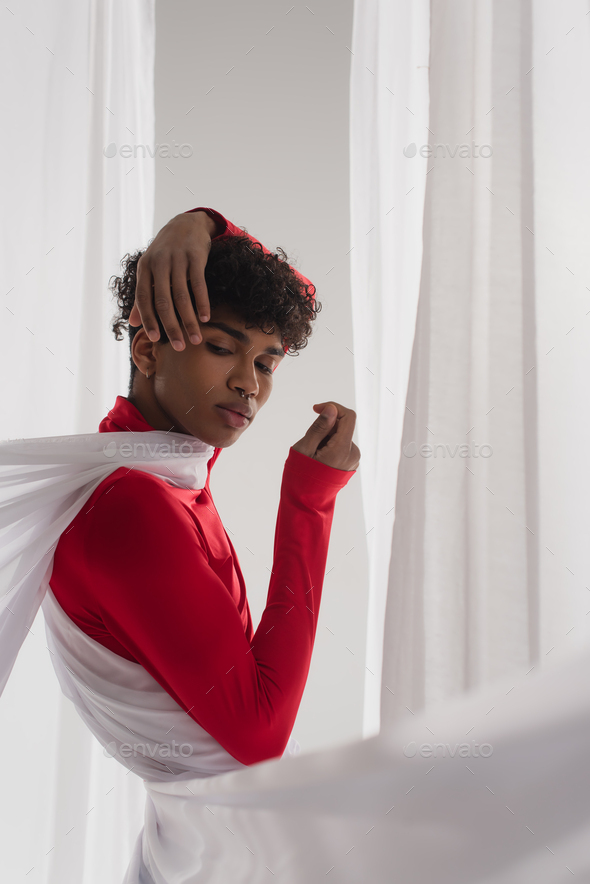 stylish african american man posing in red turtleneck near white drapery