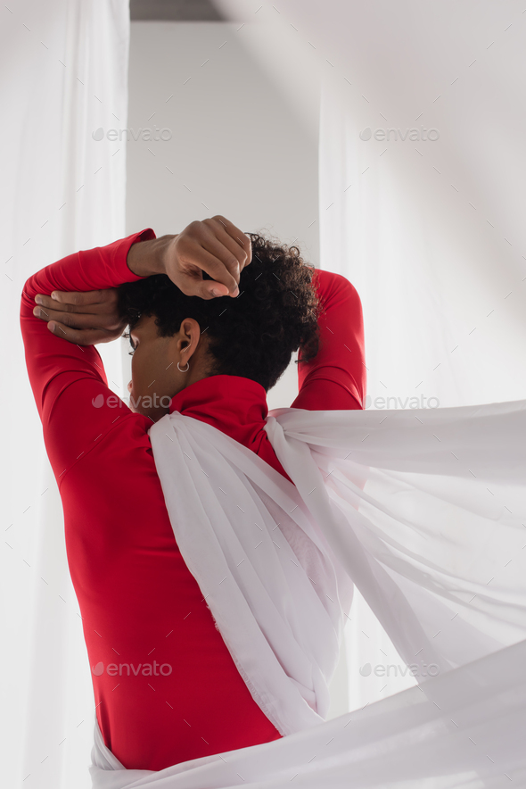 back view of african american man in red turtleneck posing in white chiffon drapery