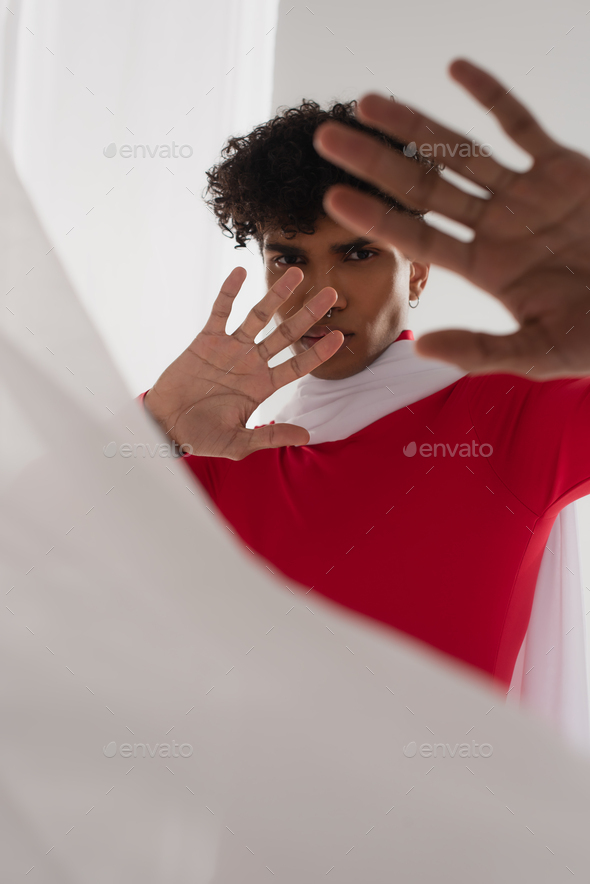 young african american man in red turtleneck showing stop gesture near white blurred cloth
