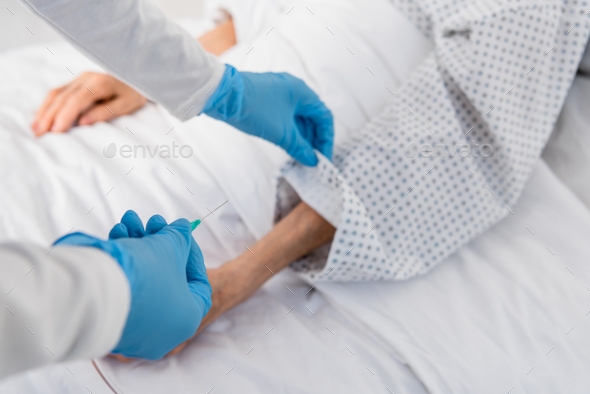 Cropped view of nurse holding needle of intravenous therapy near senior patient