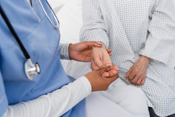 Cropped view of african american nurse checking pulse on hand of senior patient