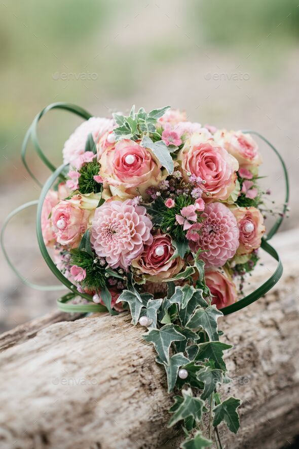 Pink bridal bouquet of roses, set atop a rustic wooden log in a