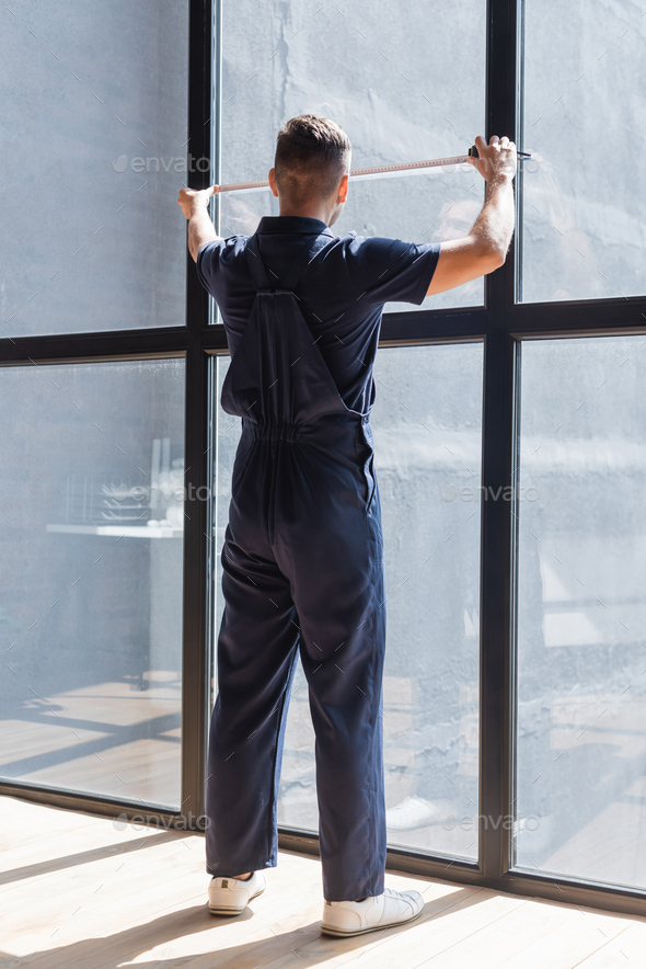 back view of workman in overalls measuring large windows Stock Photo by  LightFieldStudios