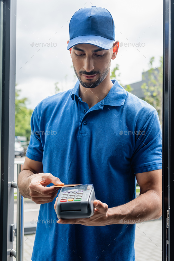 Arabian courier holding payment terminal and credit card near door