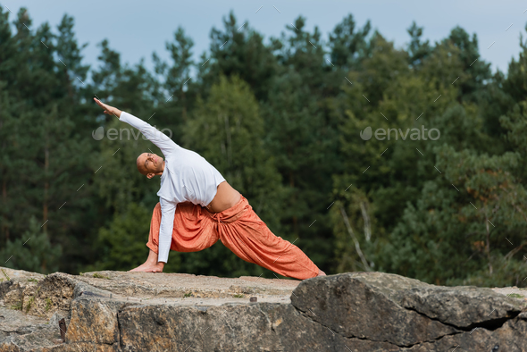 buddhist in white sweatshirt and harem pants practicing side lunge pose outdoors