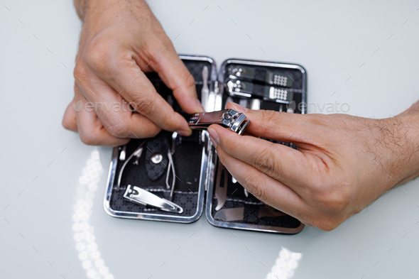Pulls nail clippers out of the manicure kit. A man gives himself a manicure
