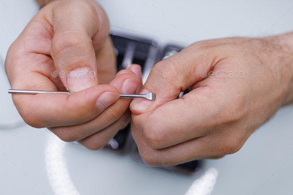 Men\'s hands clean the cuticle near the nail with a tool. A man gives himself a manicure