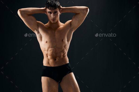 attractive sporty man with pumped up abs posing in dark studio panties