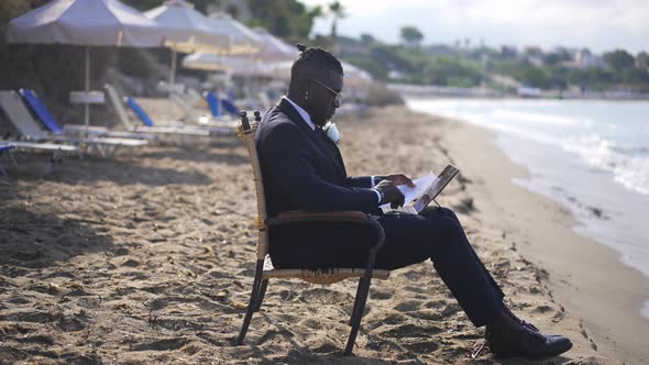 Side View Wide Shot of Busy Concentrated Handsome African American Man Messaging Online on Tablet alt