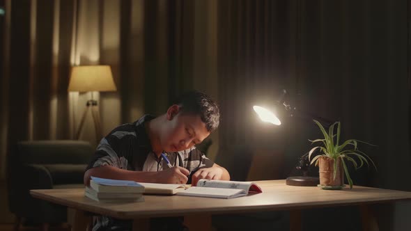 Asian Boy Is Studying At Home, Asia Child Writing While Sitting On The Table At Night alt