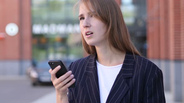 Businesswoman Reacting to Loss while Using Smartphone Outside Office alt