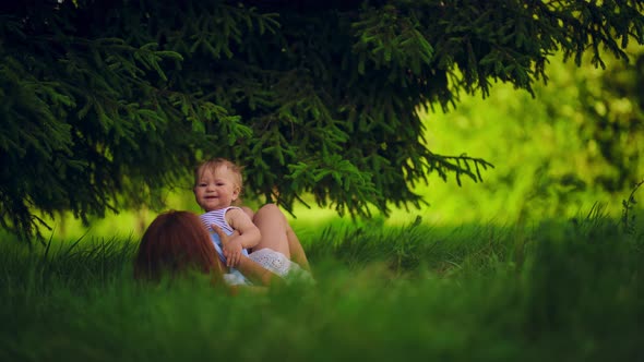 Mom with a child have fun lying in a park under a tree. alt