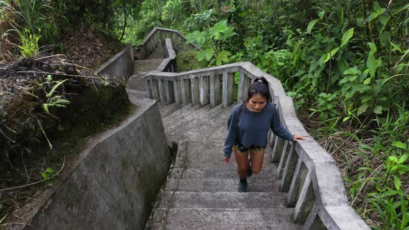 A hispanic woman with long black hair is walking up the steps of a stair alt