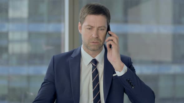 Angry Businessman Talking on Phone at Work alt