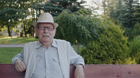 Elegant Senior Man Telling Confidently Into the Camera When Resting on Bench alt