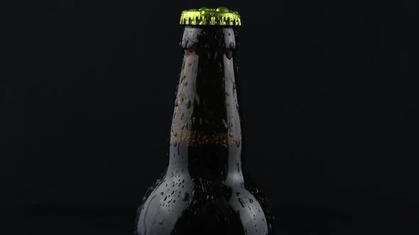 Drops of Condensate Flow Down a Beer Bottle on a Dark Background
