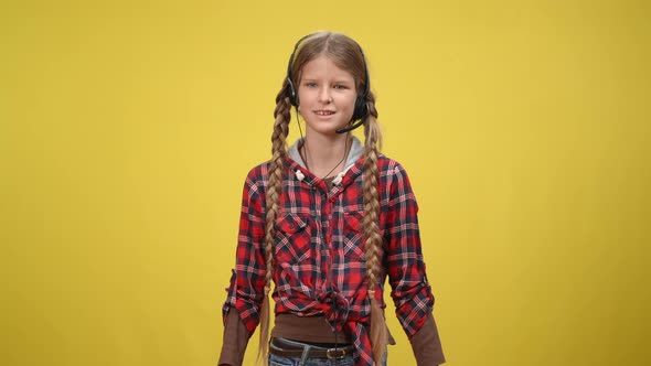 Positive Caucasian Teenage Girl in Headphones with Microphone Talking Gesturing at Yellow Background alt