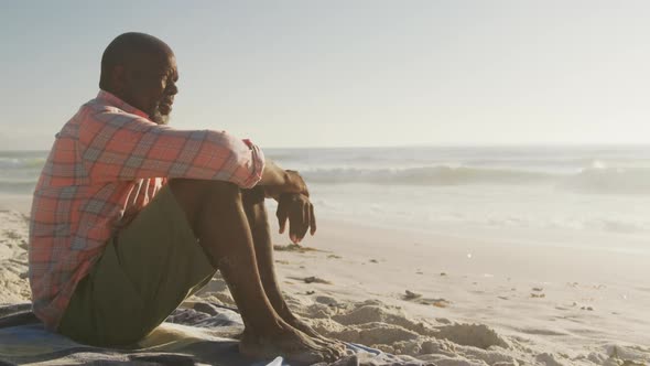 Senior african american man wearing shirt and sitting on sunny beach alt