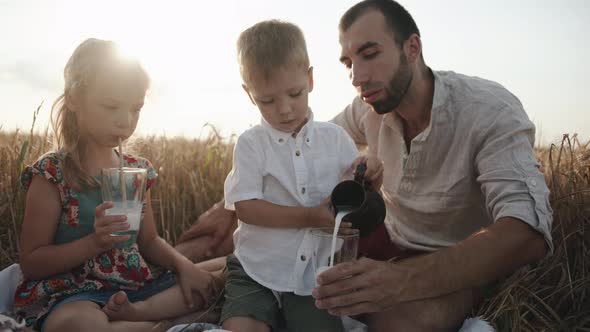 A Little Boy in a White Shirt Sits Next to His Older Sister and Pours Milk From a Jug at a Family alt