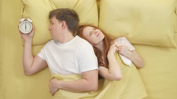 Caucasian Woman Half Asleep in Bed Irritated Hearing Alarm Clocks Partner Sleeping Next to Her