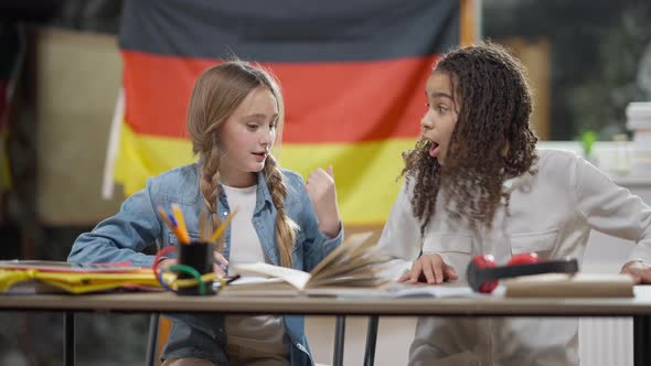Smart Genius Caucasian Schoolgirl Writing in Workbook and Declaiming As African American Classmate alt