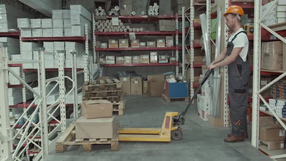 Factory Man Is Loading Cardboard Boxes on a Hand Pallet Truck in Warehouse alt