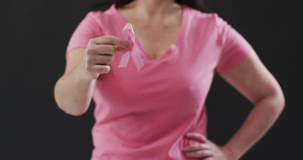 Mid section of woman holding a pink ribbon against black background alt