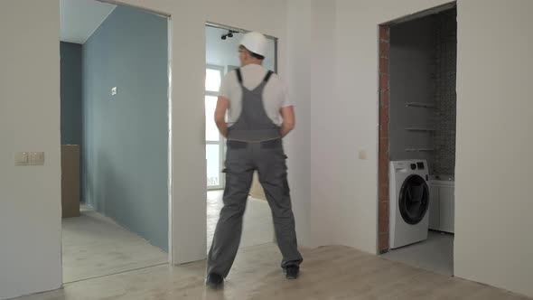 A Builder in Working Uniform Checks the Size and Quality of Doorways in a New Apartment alt