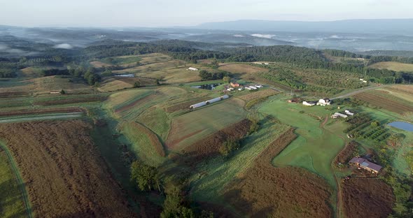 Aerial camera view of West Virginia countryside with farms, fields, mountains and fog settling in th alt