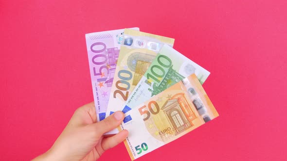 Hand in holds 50, 100, 200 and 500 EURO money bill on pink color background Counting cash banknotes