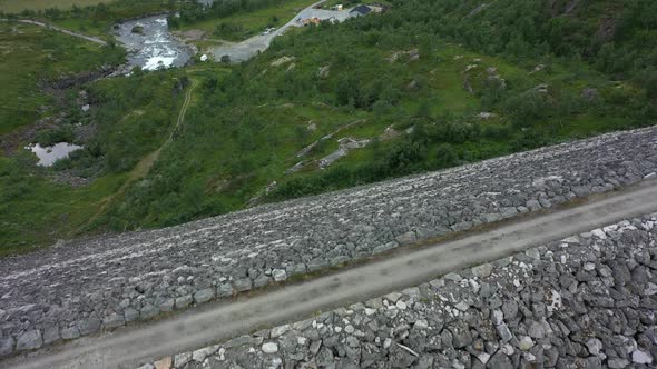 Flying over edge of massive Sysen dam at Hardangervidda national park Norway - Rocky landfill embank alt