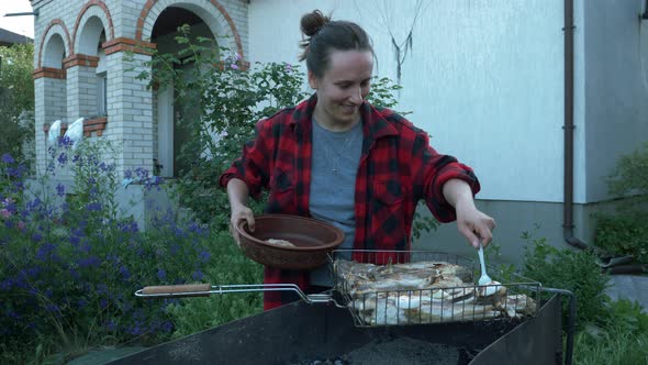 Woman puts cooked on barbecue grilled fish in plate on yard of summer house. Preparing fish on grill alt