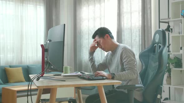 Asian Man Being Tired While Using The Desktop Computer For Working At Home alt