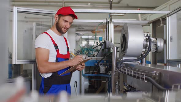 Young Factory Man in Uniform Making Notes on Clipboard at Water Production Factory