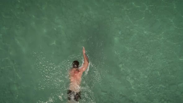 Aerial view of a man swimming in transparent water in Syros island, Greece. alt