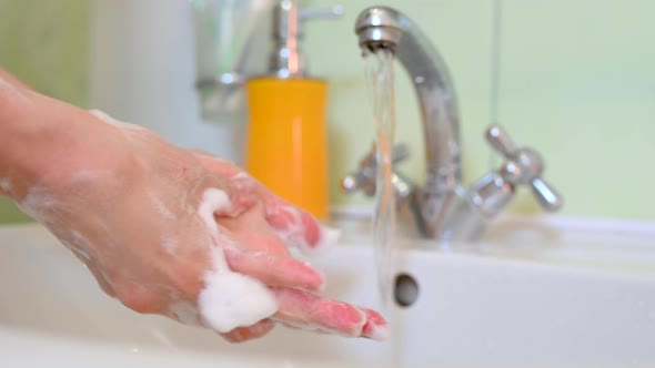 Woman washing her hands with soap in the bathroom.