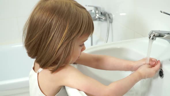 Little Girl Washes Hands with Antibacterial Soap Looks at Camera Laughs and Smiles