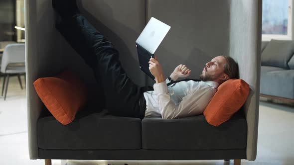 Office Manager Lies in a Large Chair and Works at a Laptop Office Work in an Open Space a Man Types alt