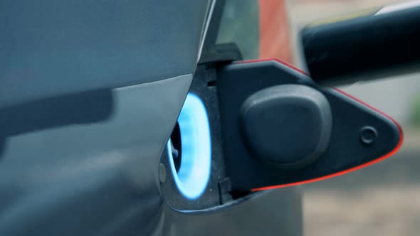 Filler Hole of an Electrocar Opens and a Fuelling Nozzle Is Getting Inserted Into It alt