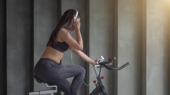 Girl Cycling in Gym and Listening to Music from Headphones alt