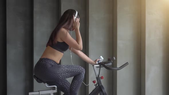 Girl Cycling in Gym and Listening to Music from Headphones