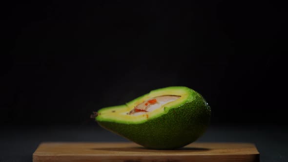 Cutted Avocado at Black Background with Water Droplets Falling in Slow Motion on Tropical Fruit alt
