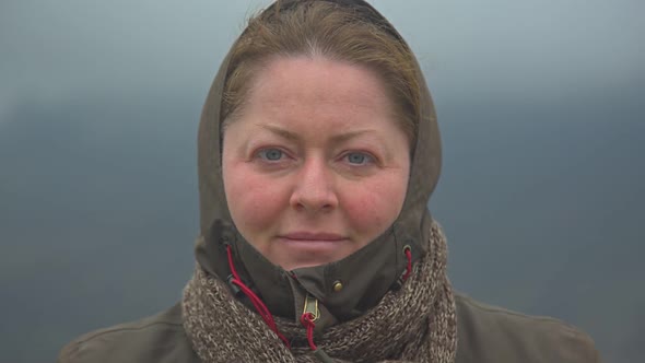 A Beautiful Middleaged Woman with Gray Eyes Stands Against the Background of the Misty Mountains alt