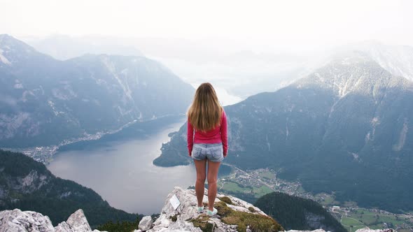 Young Woman Standing on Mountain Top and Contemplating Beautiful View of Mountain Lake alt